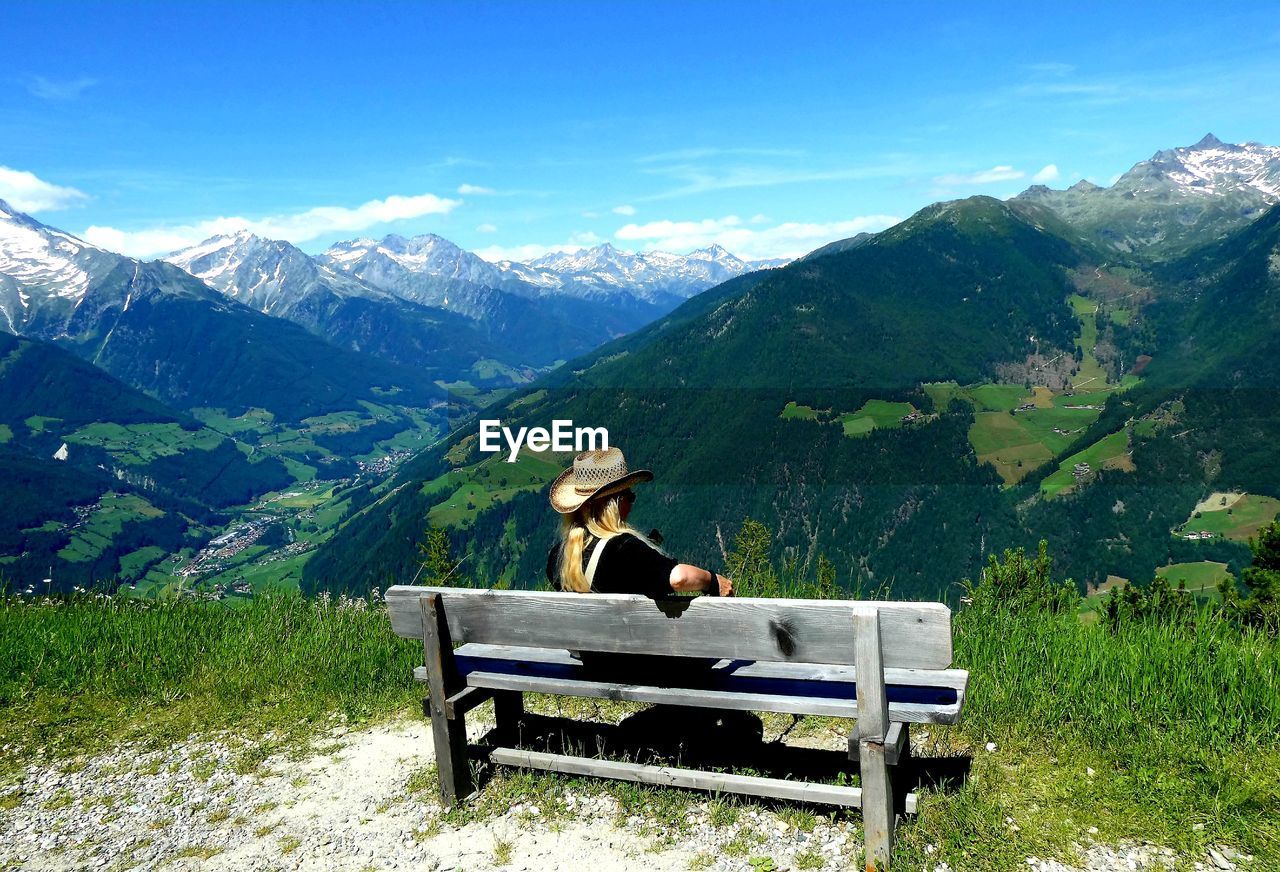 Young woman sitting on seat in mountains against sky