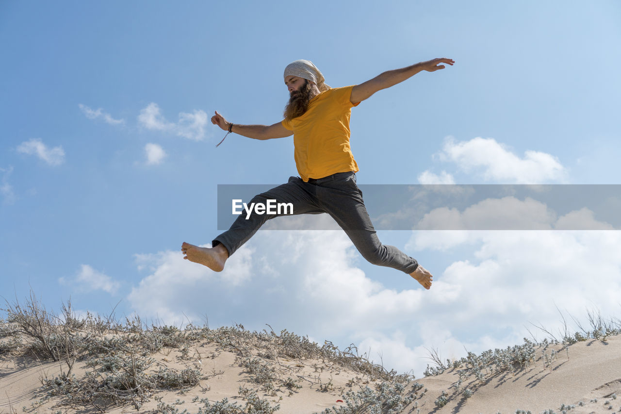 Carefree man with arms outstretched jumping on sand at beach