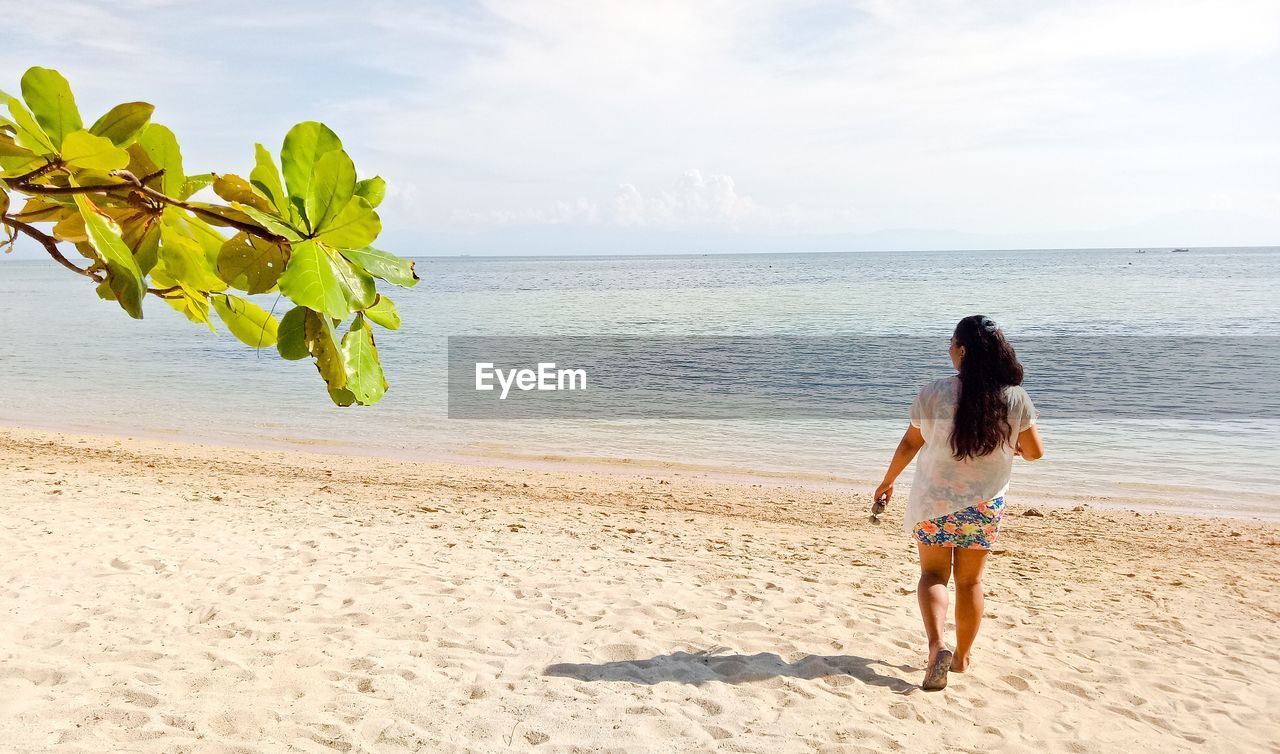 Rear view of woman walking at beach against sky