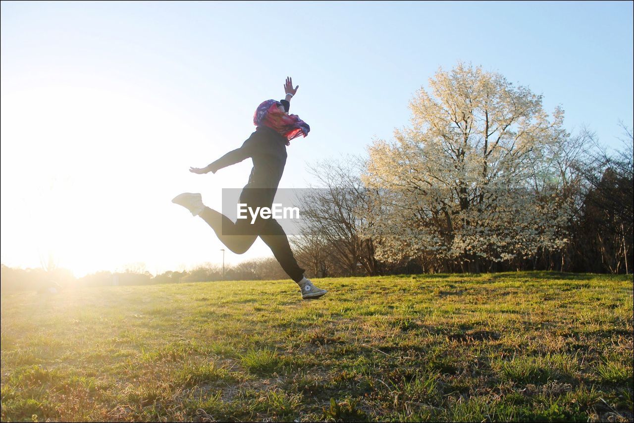 GIRL JUMPING ON FIELD AGAINST CLEAR SKY