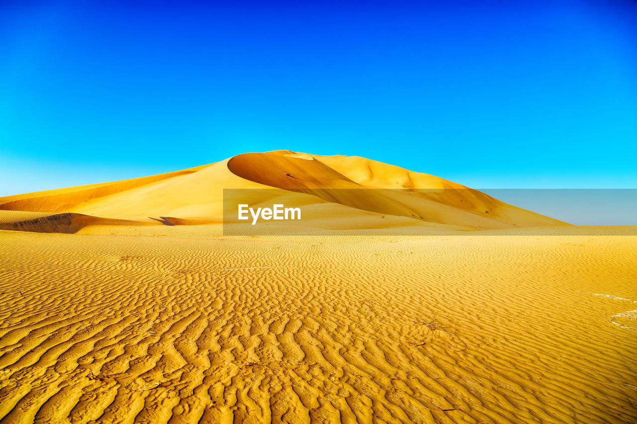 Sand dunes in desert against clear blue sky