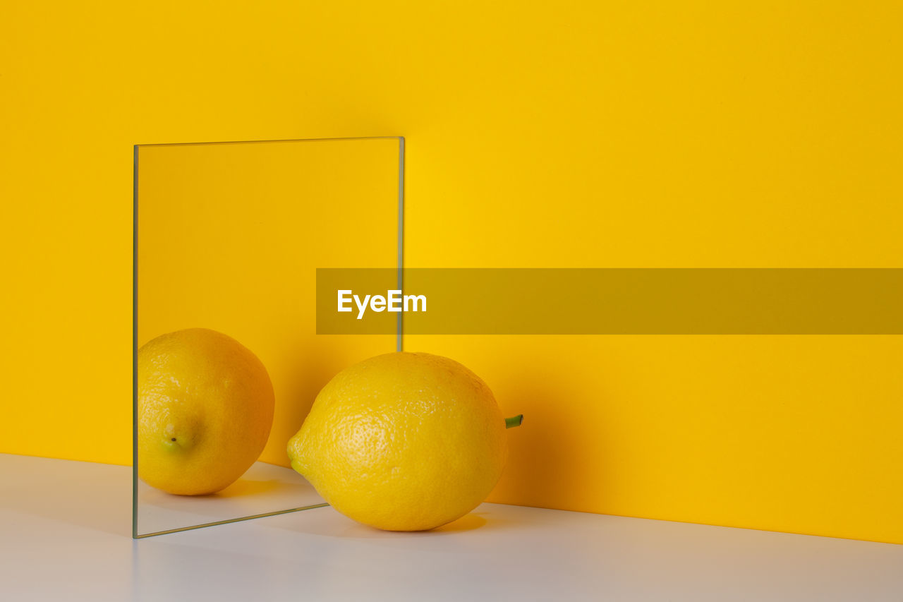 Yellow lemon is reflected in a mirror on a yellow background