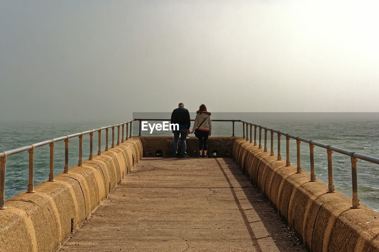 Couple standing on pier over river during foggy weather