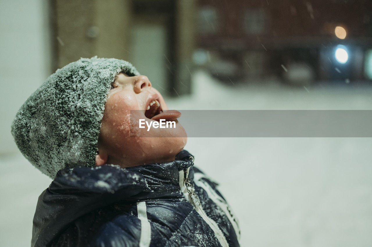 Happy boy catching snow with tongue in winter