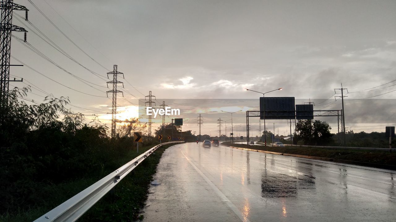 WET ROAD BY CITY AGAINST SKY