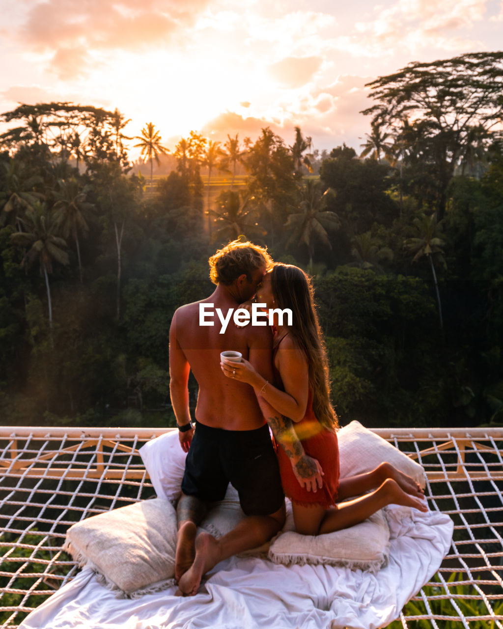 Couple sitting in a hummock above jungle in balo, drinking coffee