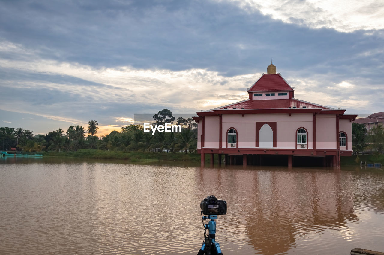 water, architecture, sky, cloud, built structure, reflection, building exterior, nature, building, lake, vacation, travel destinations, religion, one person, travel, outdoors, landscape, place of worship, beauty in nature, belief, environment, sunset, city, waterway, tourism, beach, childhood, history, day, evening, tranquility, house, tree, the past, scenics - nature