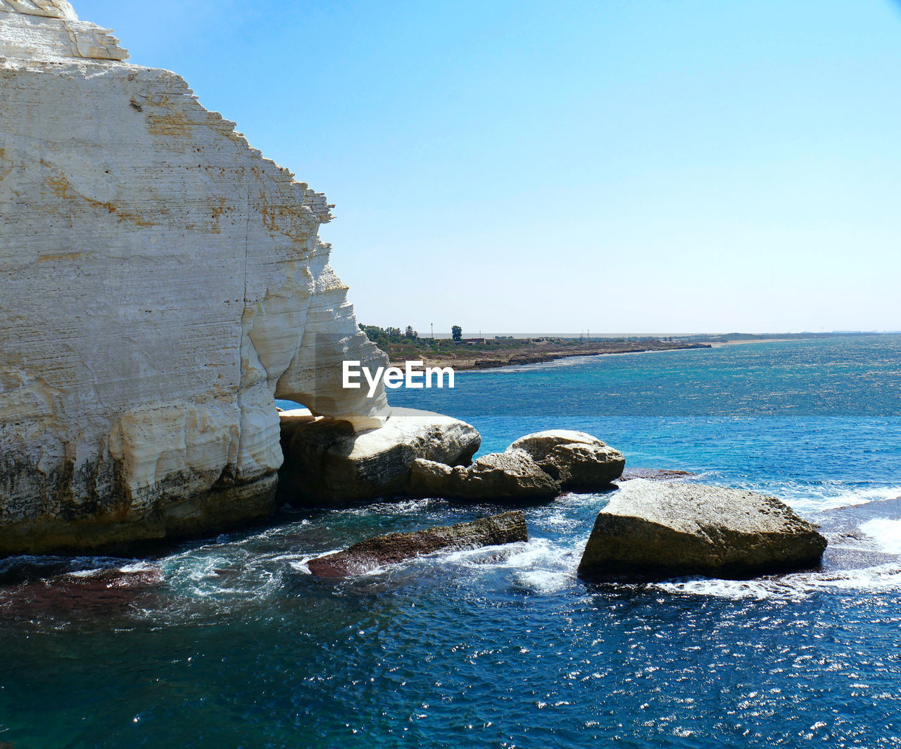 Rocks in sea against clear blue sky