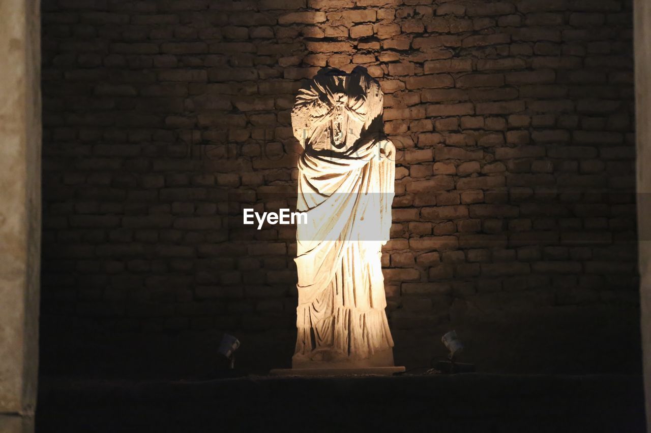 CLOSE-UP OF STATUE AGAINST STONE WALL AT NIGHT