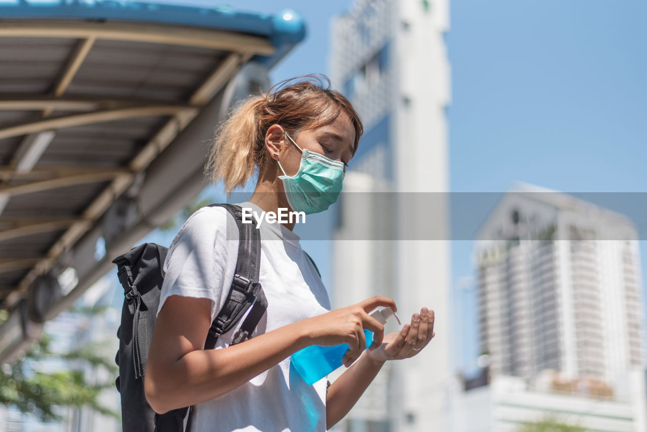 Young woman wearing mask washing hands in city