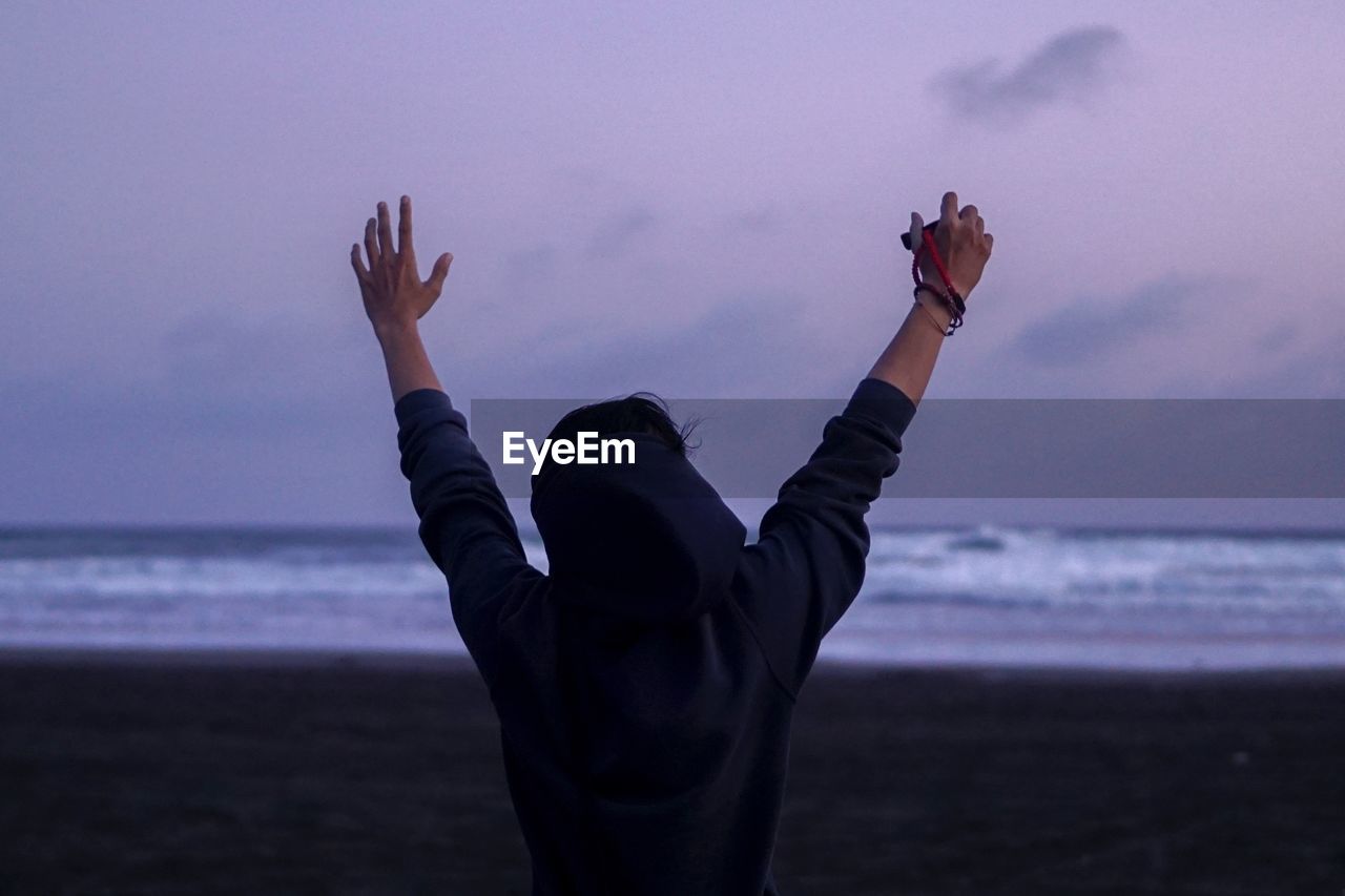 Rear view of person with arms raised standing at parangtritis beach during dusk