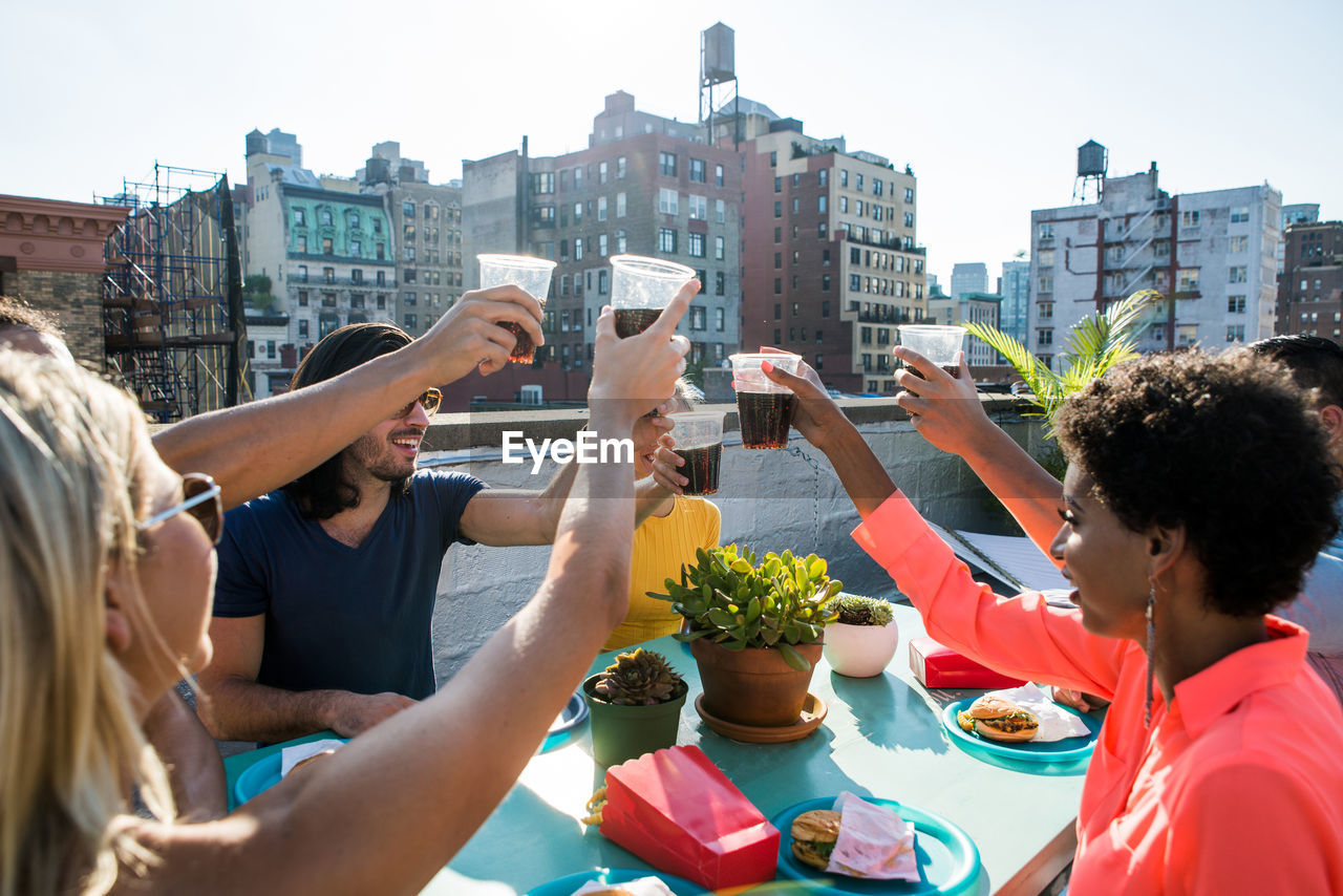 Friends toasting drinks while sitting on building terrace in city