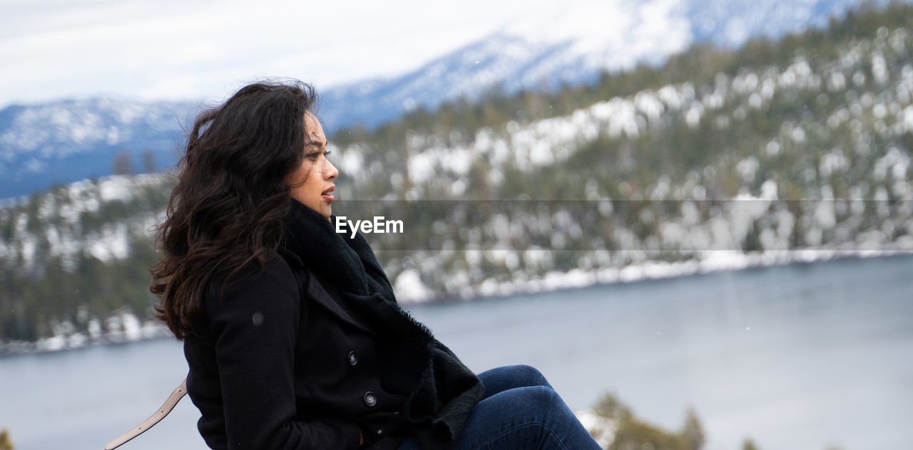 Woman looking away while sitting on land in winter