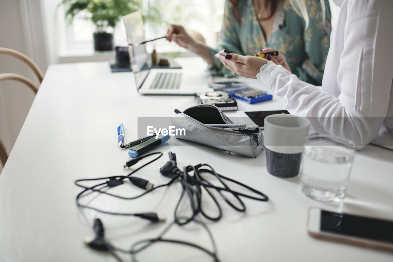 Midsection of female colleagues working on hard drive at table in home office