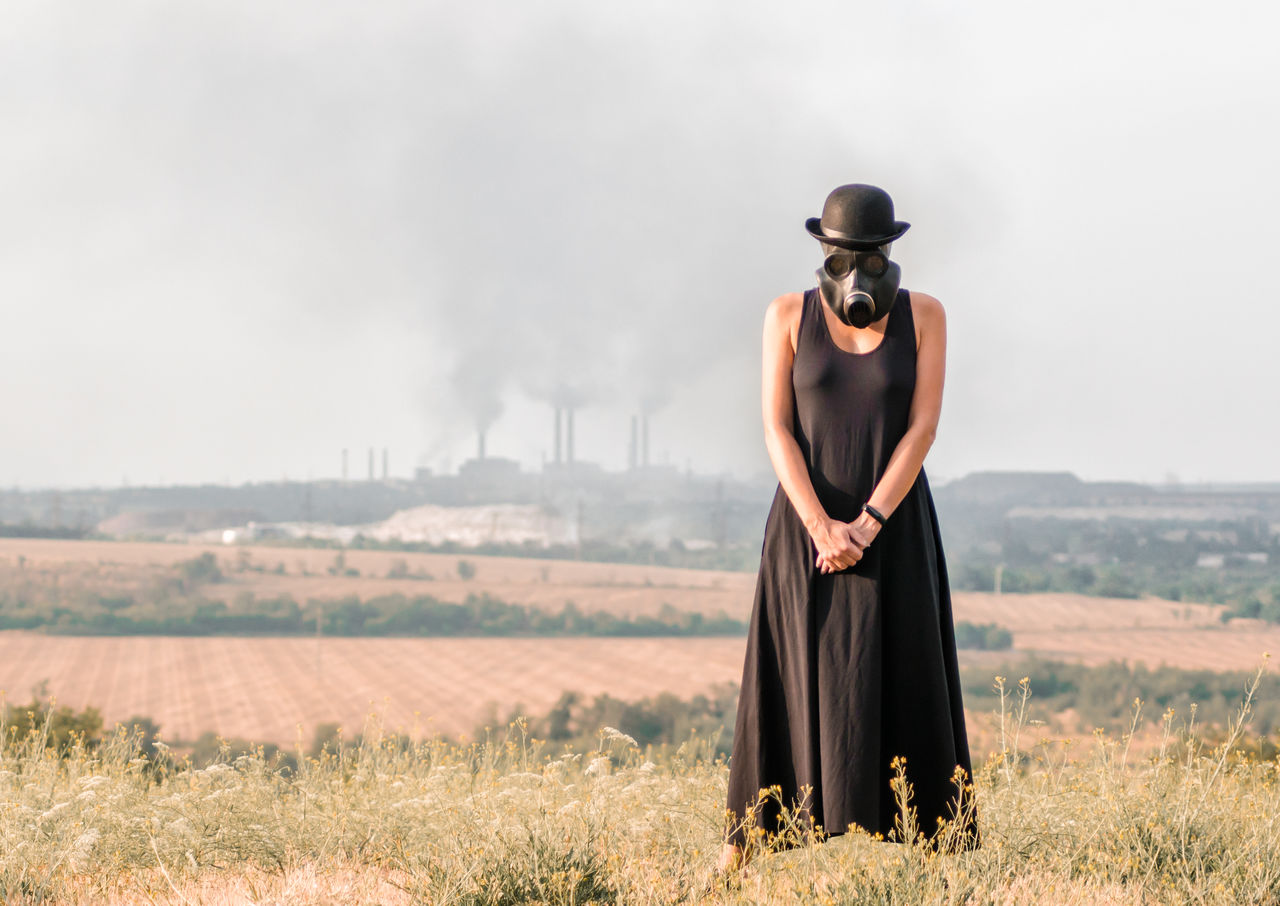 Woman wearing gas mask standing on land against sky