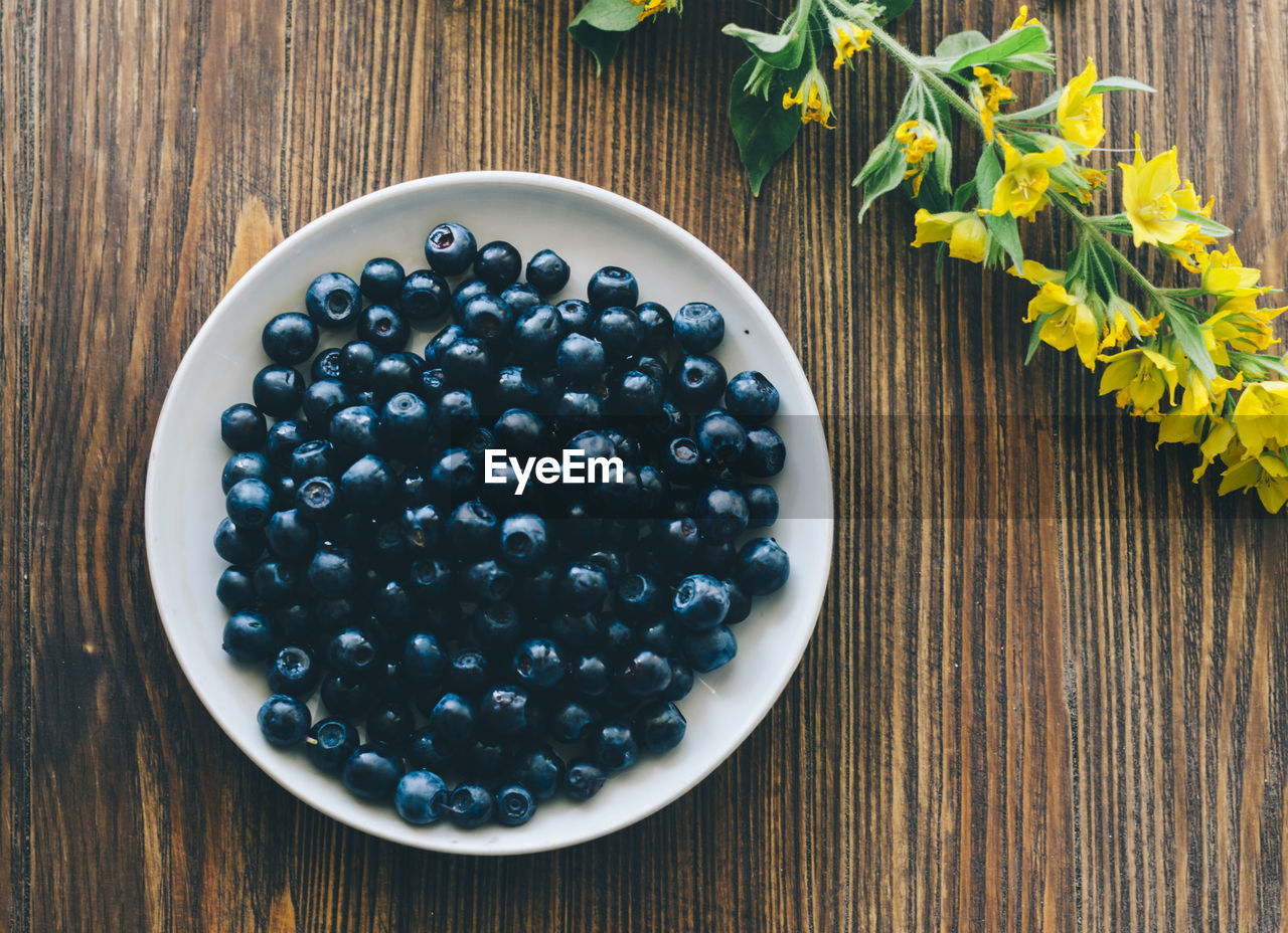 Directly above shot of blueberries in plate by yellow flowers on table