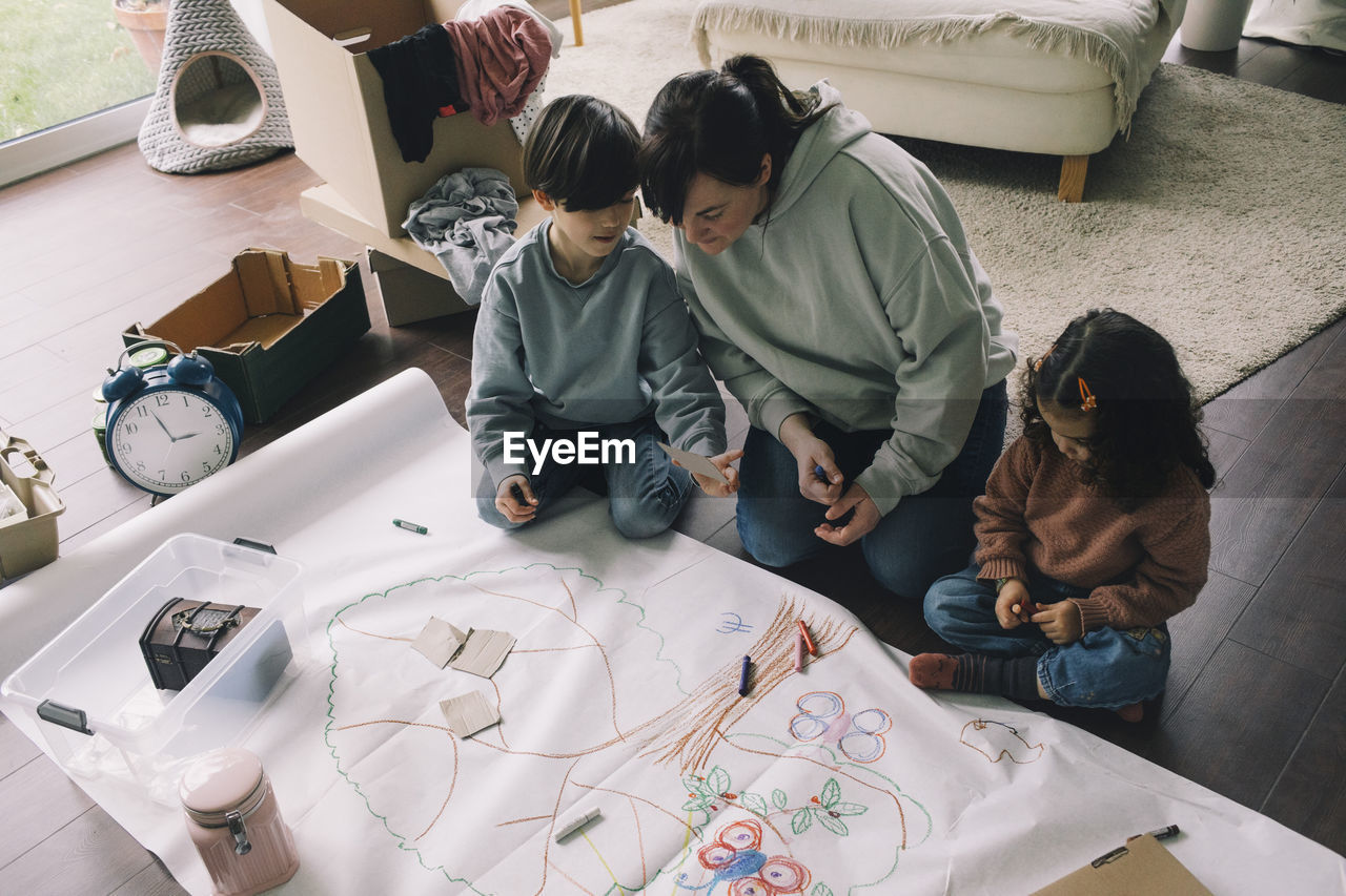 Mother with son and daughter drawing tree on cloth in living room at home