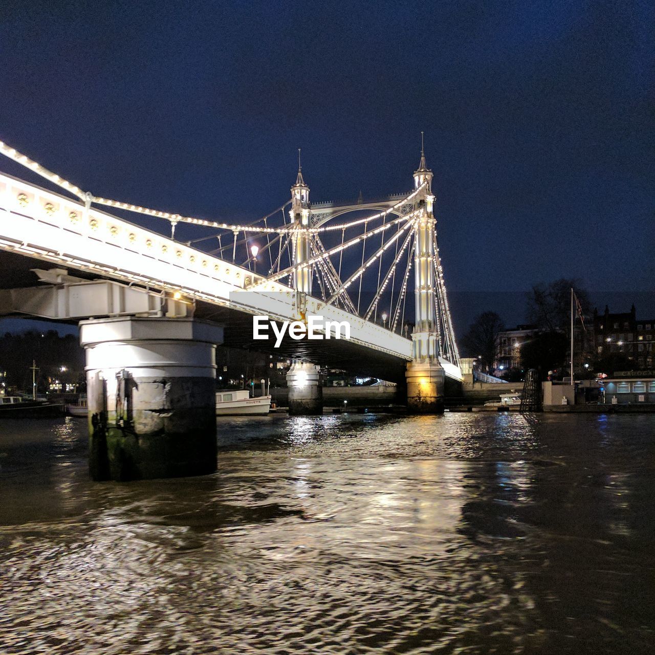 VIEW OF ILLUMINATED BRIDGE OVER RIVER AT NIGHT