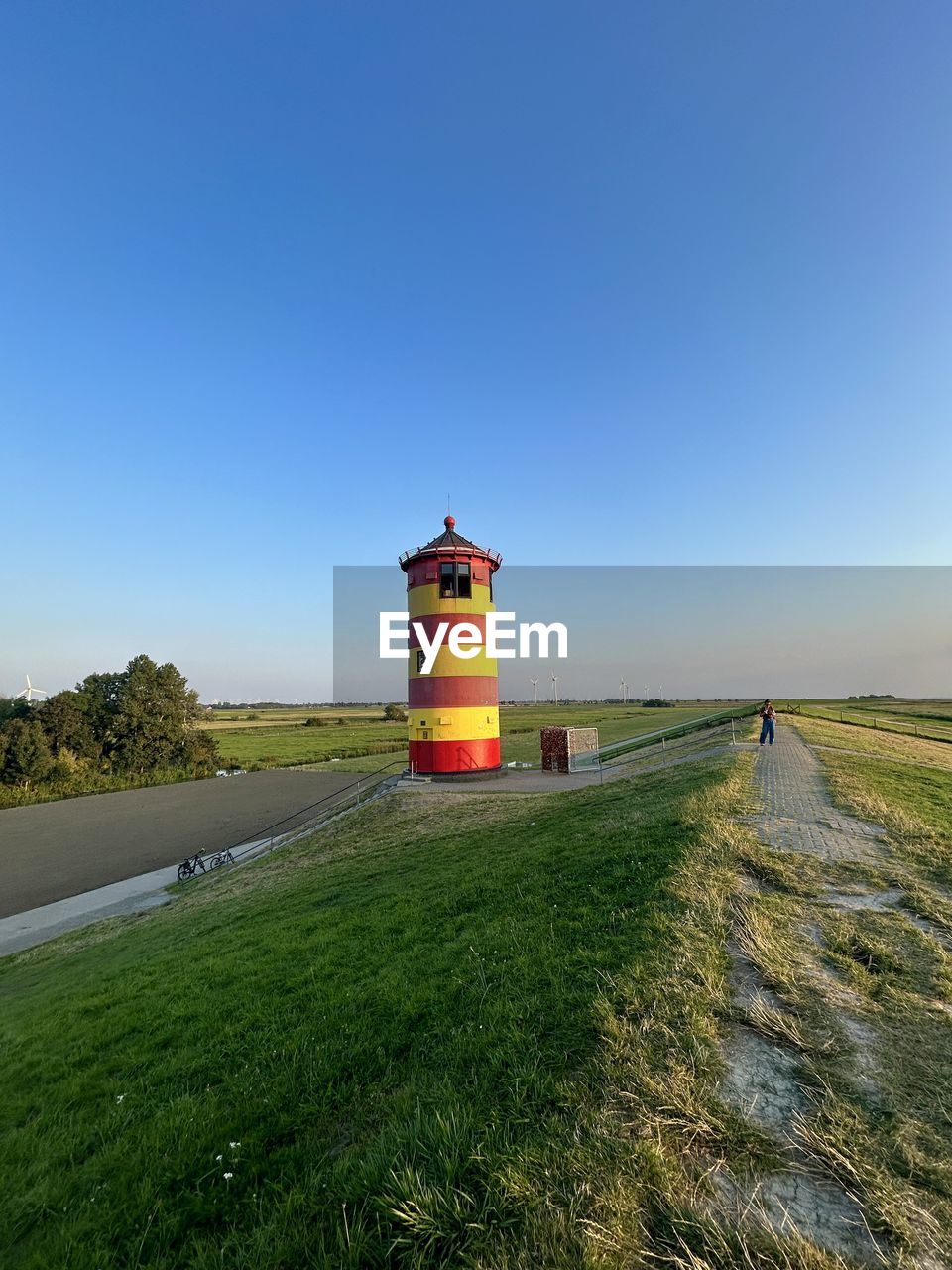 sky, lighthouse, tower, architecture, guidance, built structure, nature, grass, coast, land, landscape, building exterior, security, plant, environment, protection, blue, clear sky, no people, sea, building, water, horizon, scenics - nature, day, beach, travel, outdoors, transportation, road, travel destinations, field, rural scene, copy space, hill, tranquility, non-urban scene, rural area, sunny, beauty in nature, footpath, sunlight