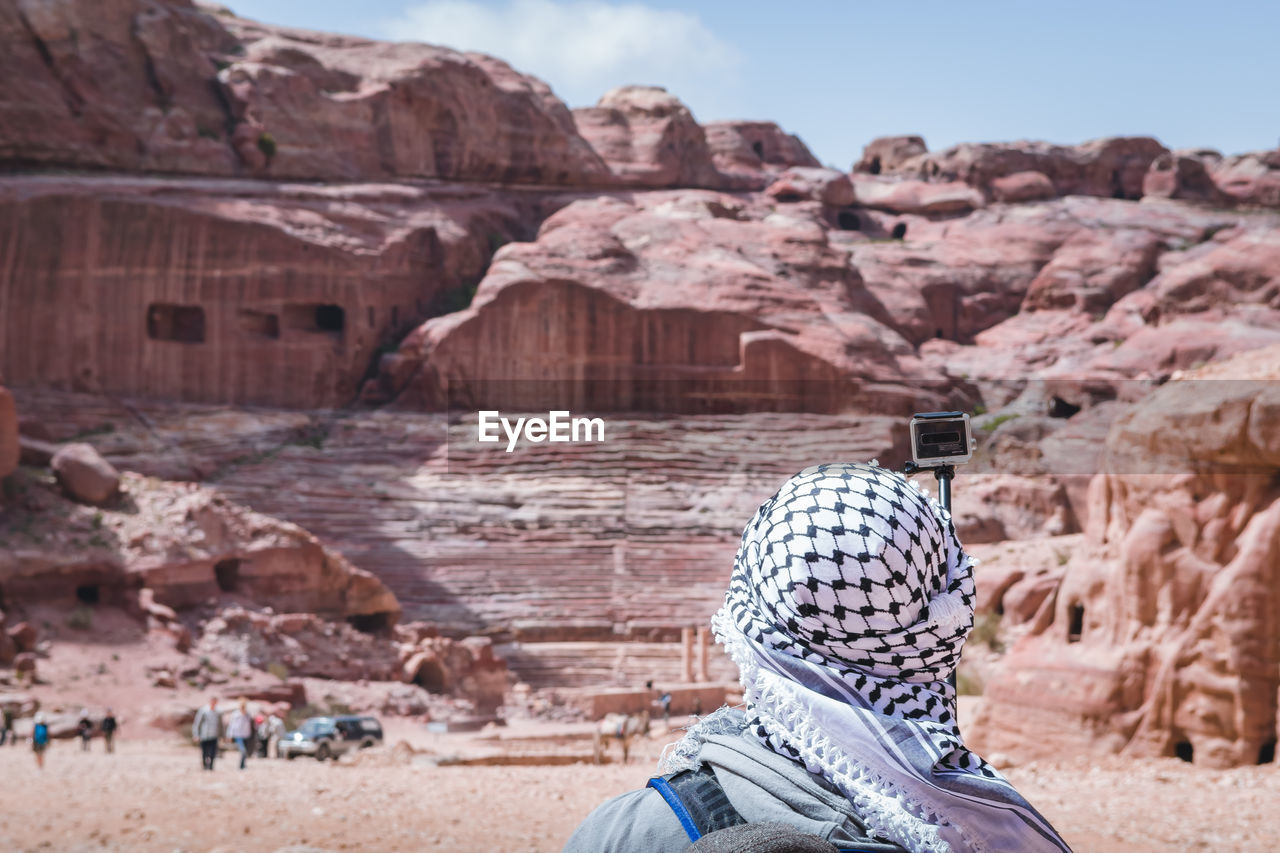 Rear view of woman taking selfie with camera wile standing against rock formation
