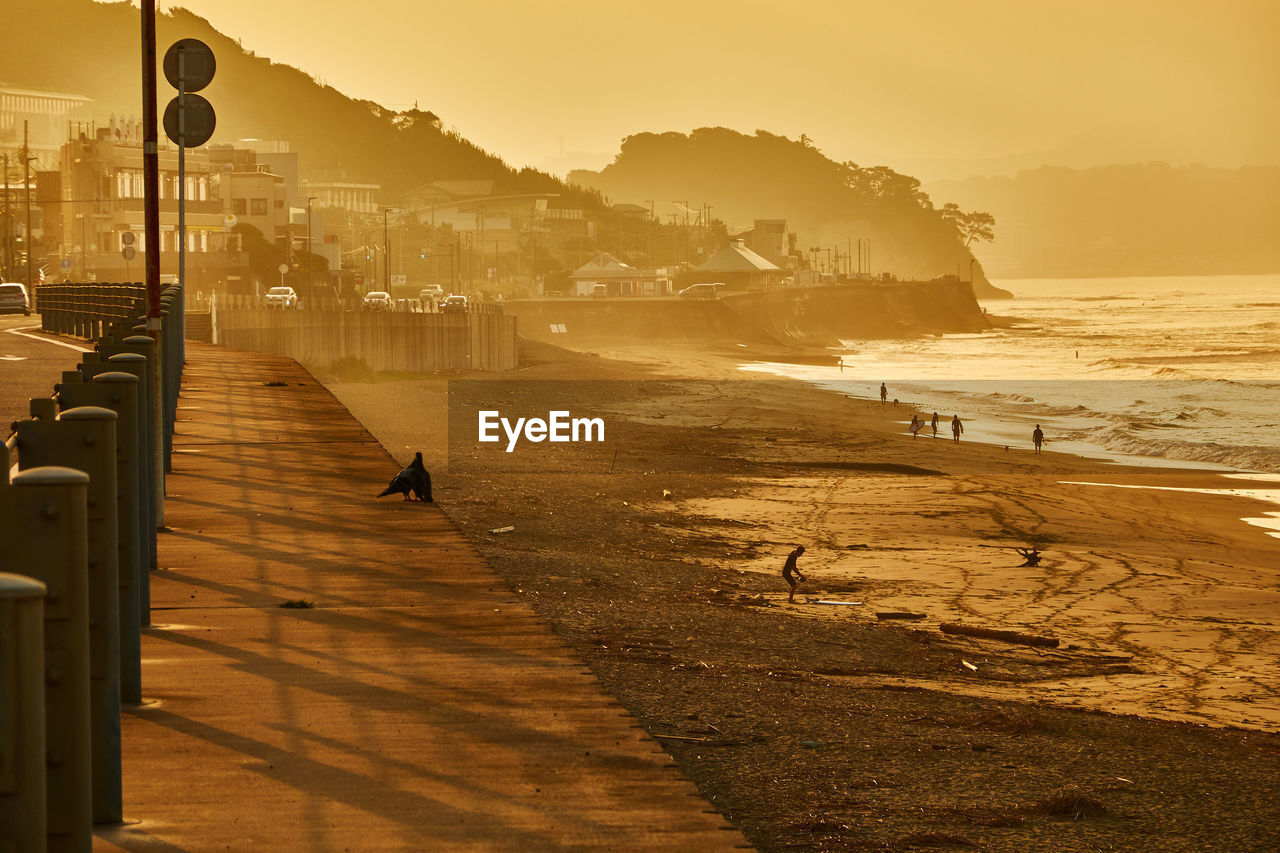 Scenic view of beach with silhouette people against orange sky during sunrise