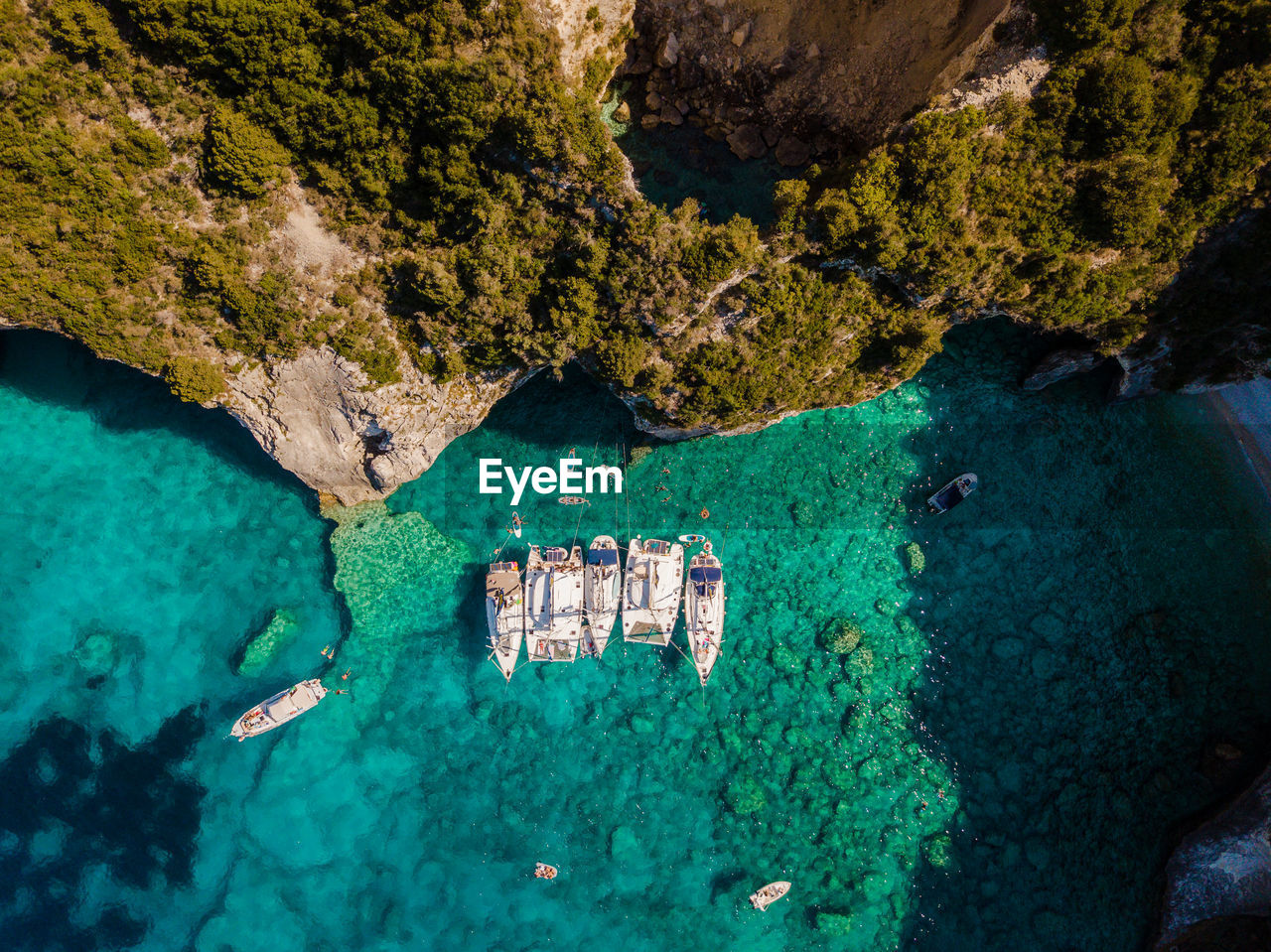 Anchored sailboats in turquise blue by near large sea caves in paxos island greece. 