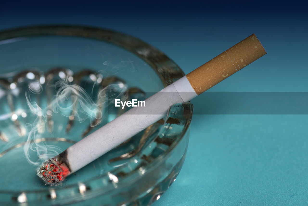 Close-up of cigarette in ashtray on blue background