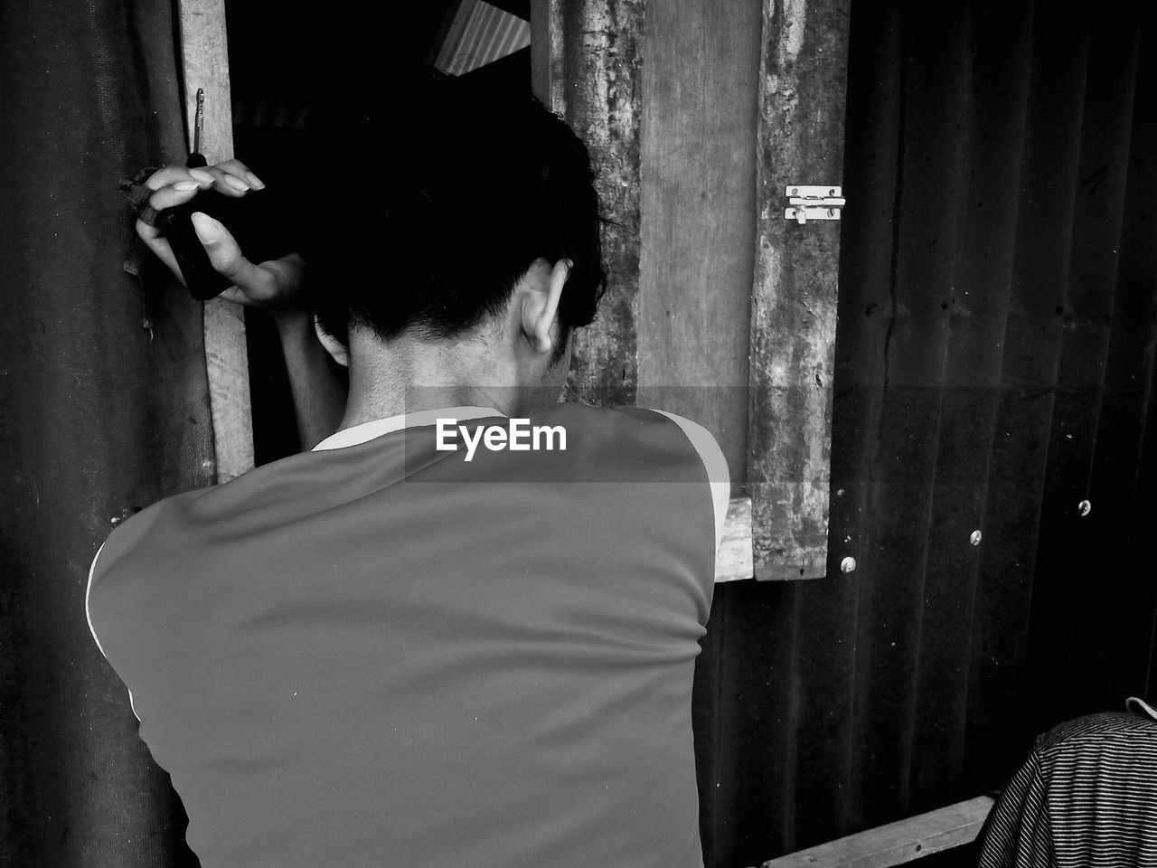 Rear view of man leaning on corrugated wall by window