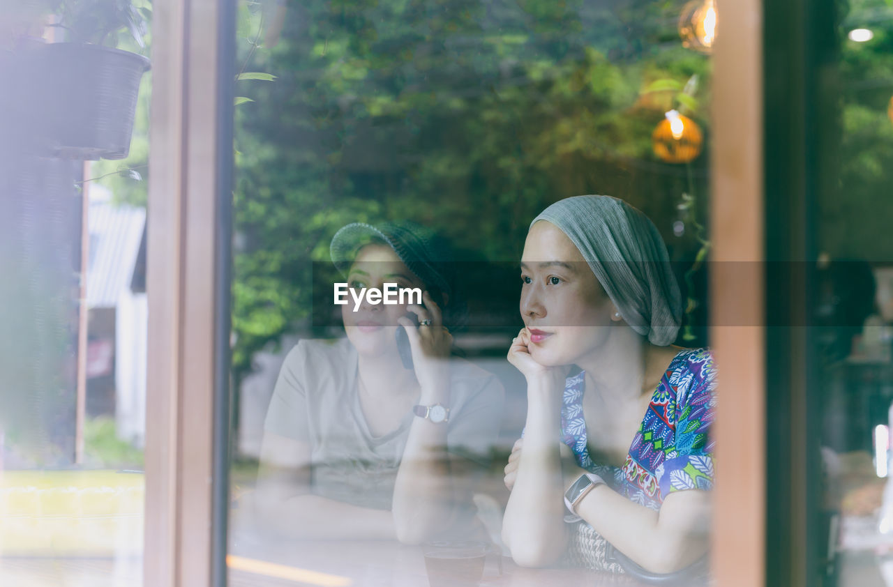 Two woman have coffee together in cafe, view through window glass.