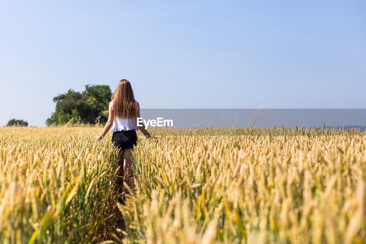 REAR VIEW OF WOMAN STANDING ON FIELD