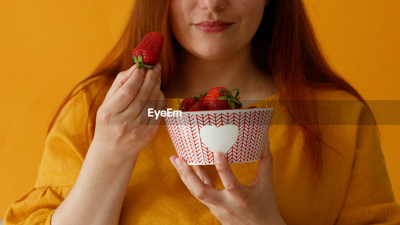 Midsection of woman holding strawberry against white background