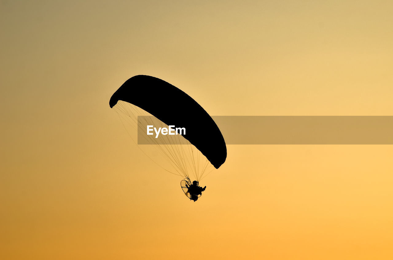Low angle view of silhouette paragliding against clear sky during sunset