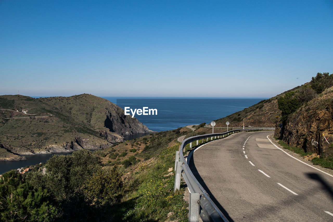 Scenic view of road by sea against clear blue sky