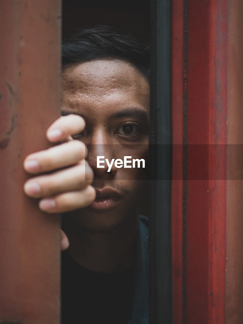 Close-up portrait of young man peeking through door