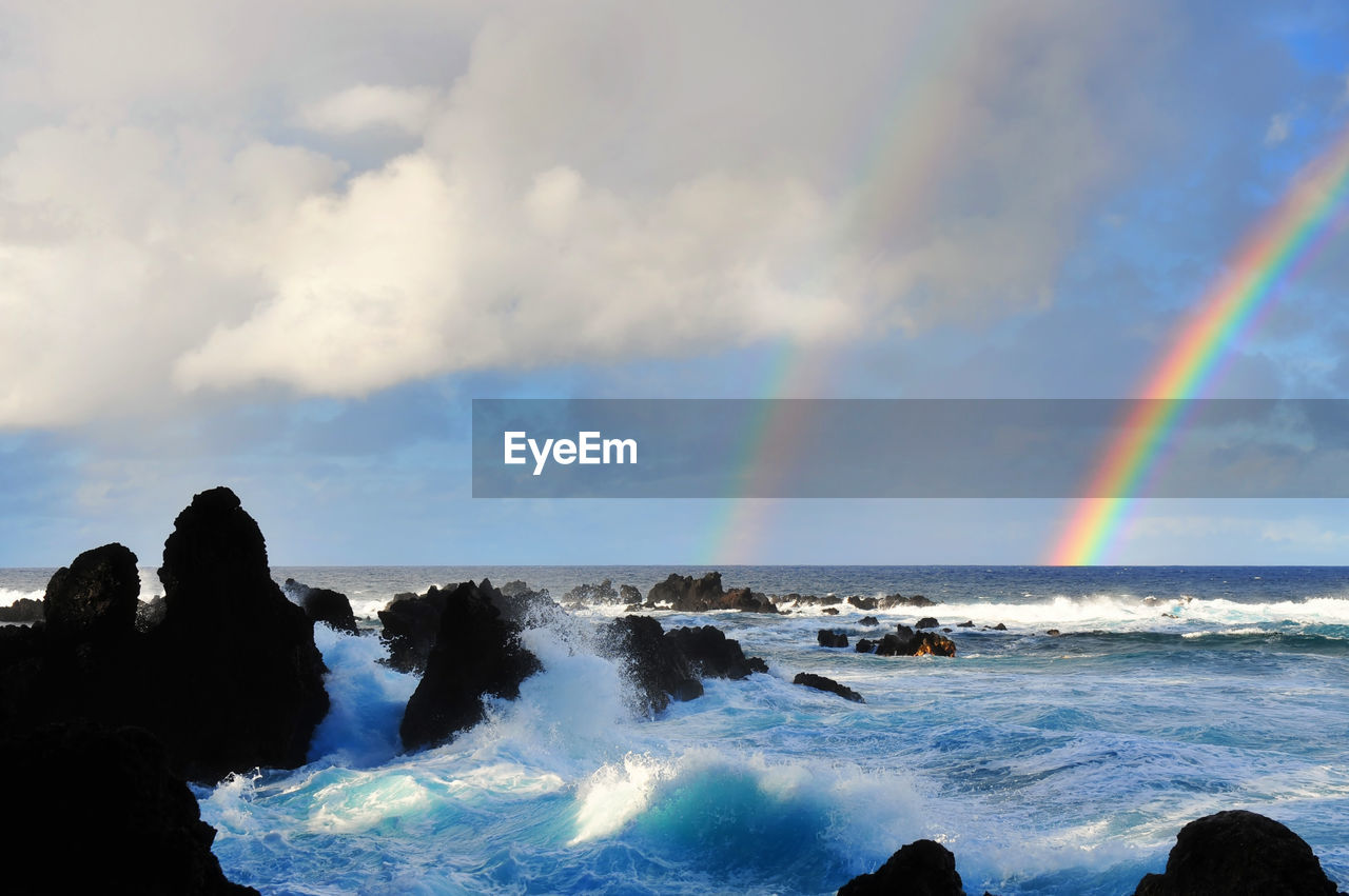 Scenic view of rainbow over sea against cloudy sky