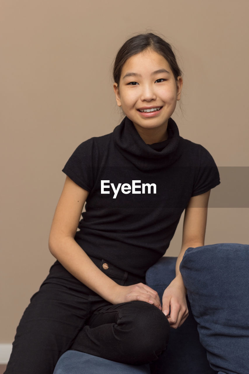 Portrait of smiling young woman sitting against wall