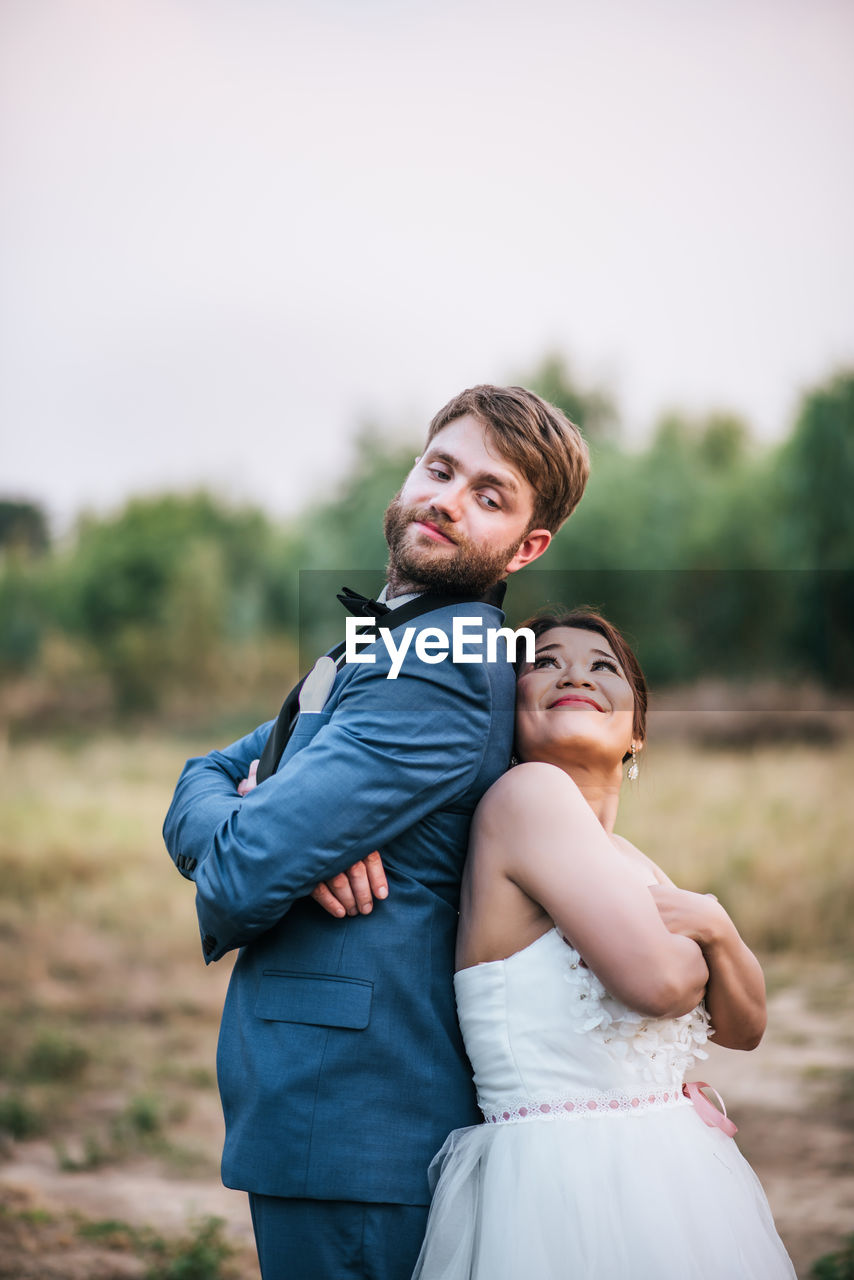 Smiling newlywed couple embracing on field