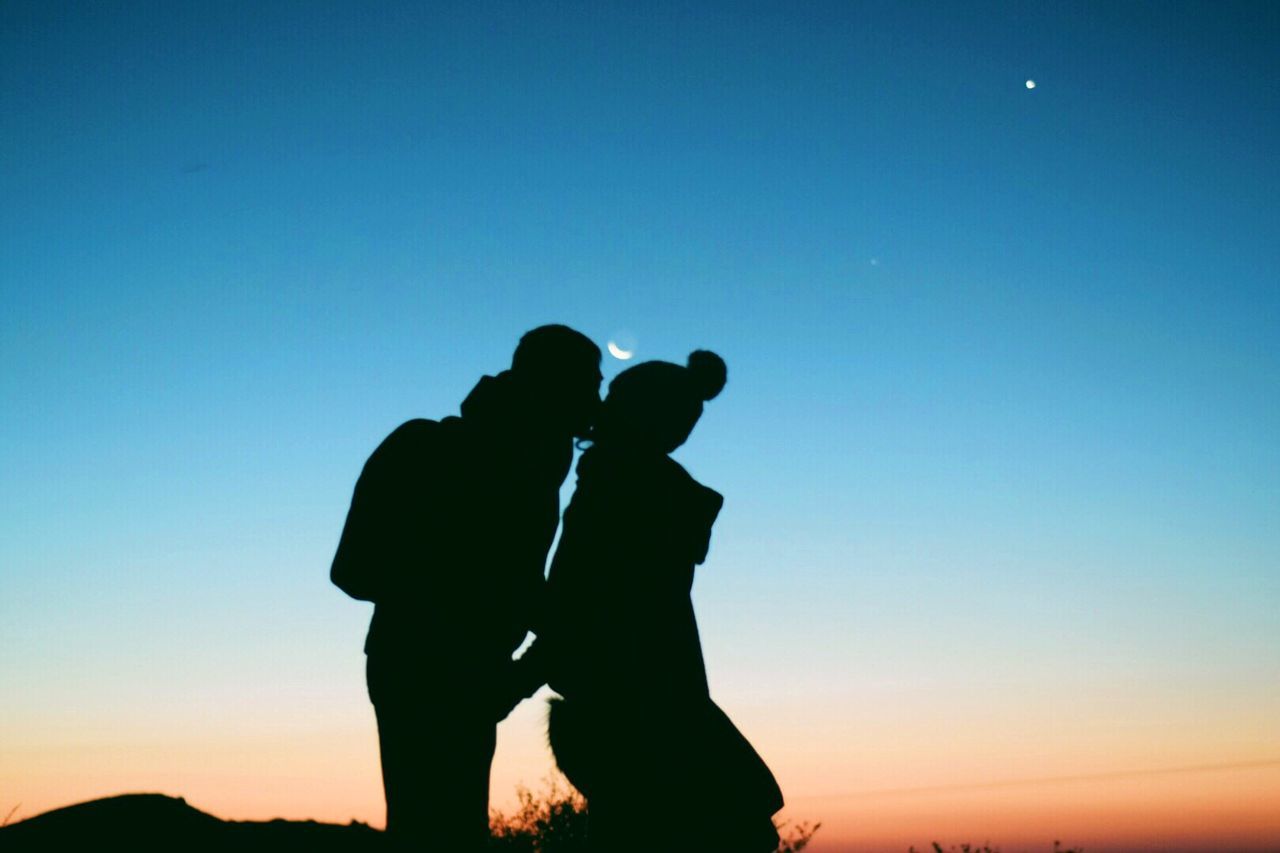 Silhouette couple standing against sky at dusk