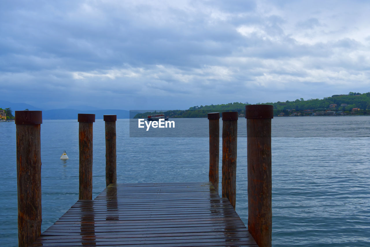 Wooden jetty at a lake with ferry in the background in a cloudy day