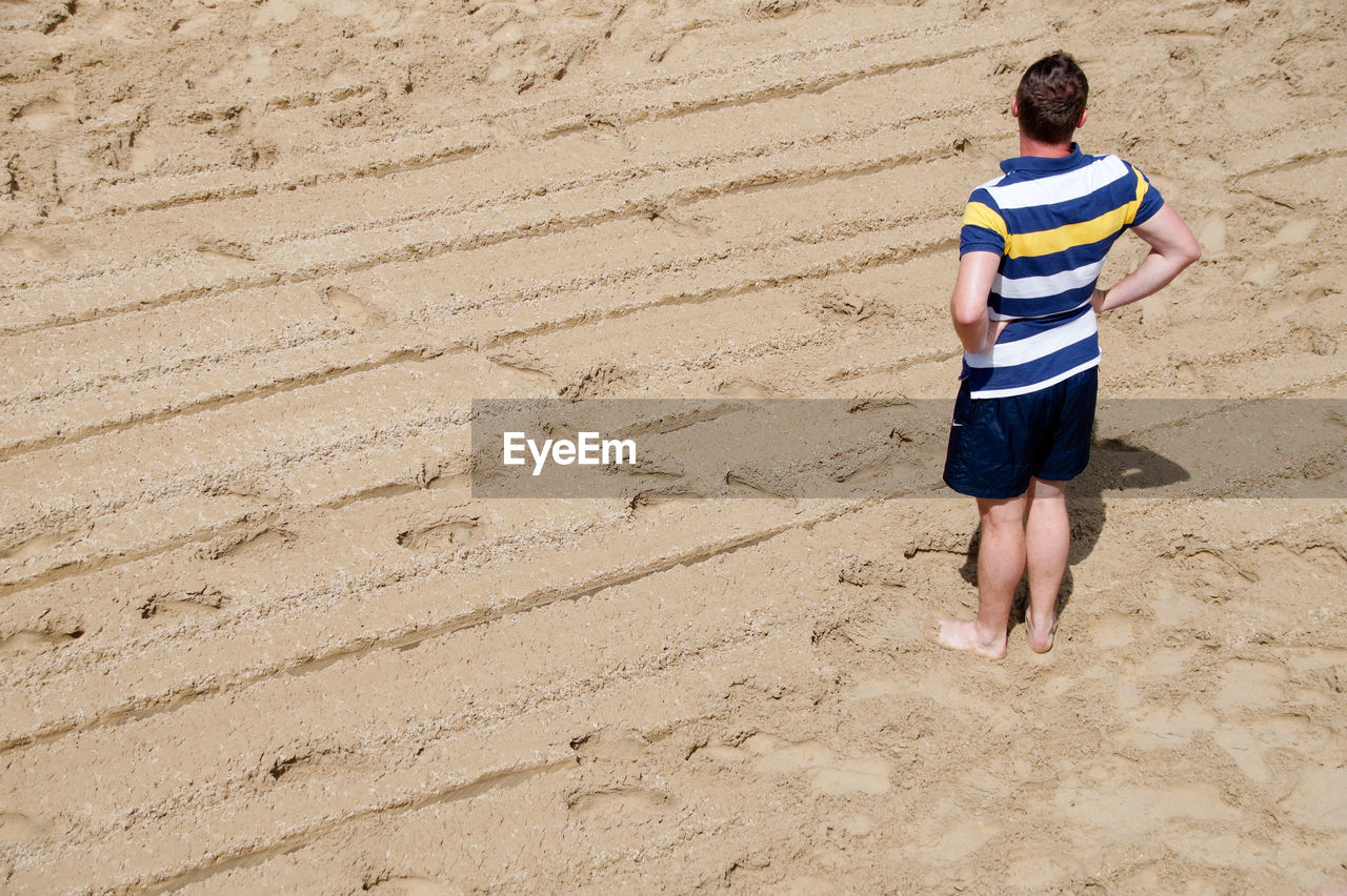 High angle view of man standing on sand at beach during sunny day