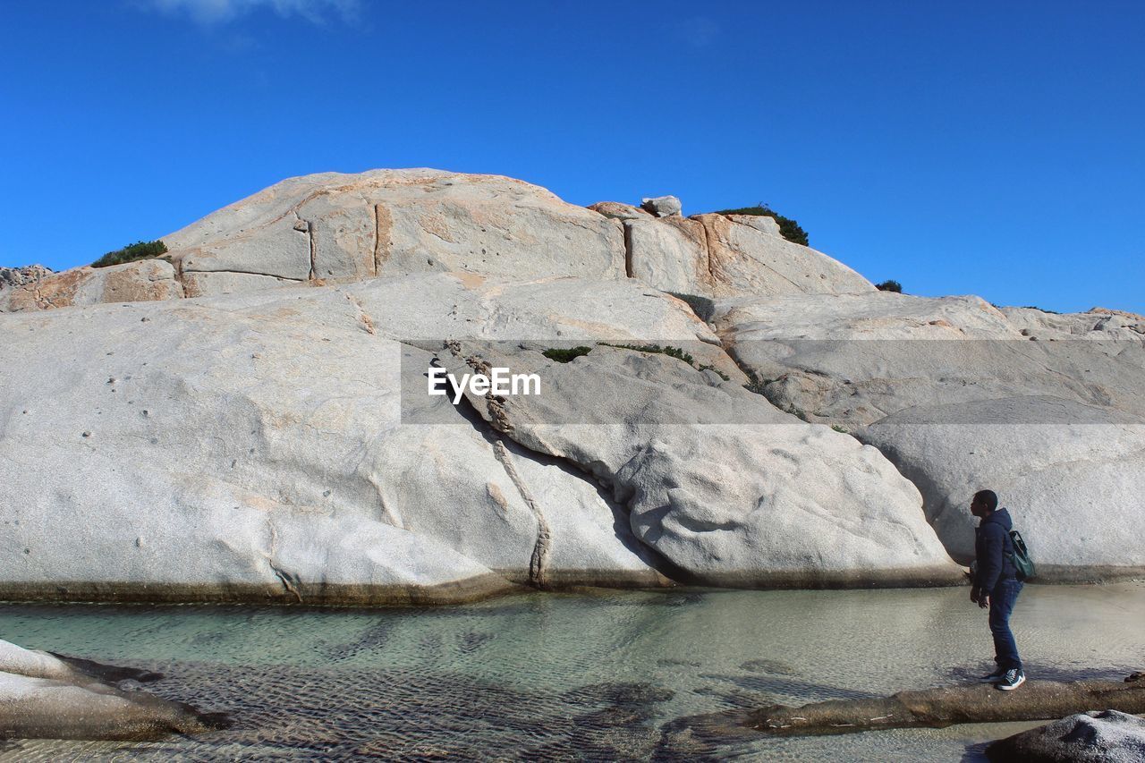 Man standing by rock formation at beach in la maddalena