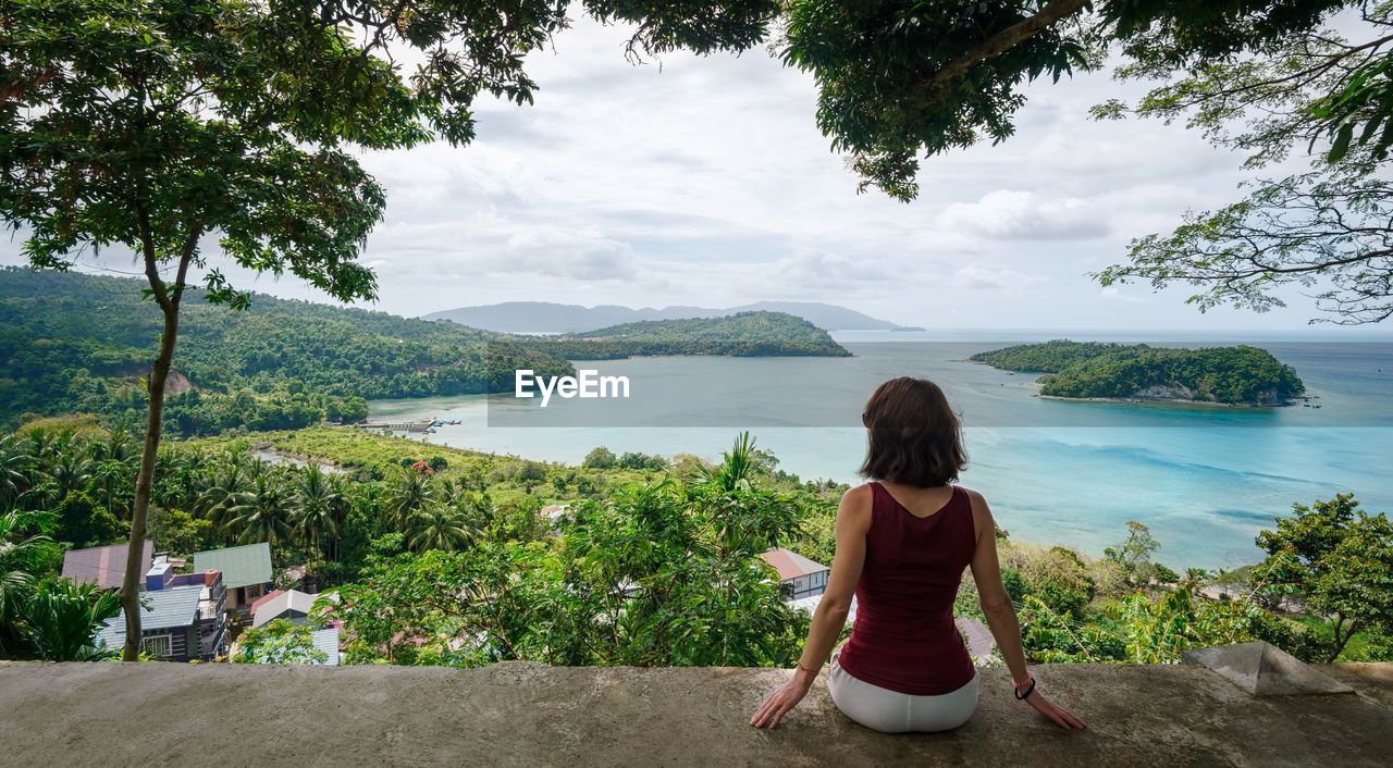 Rear view of woman sitting on railing against sea