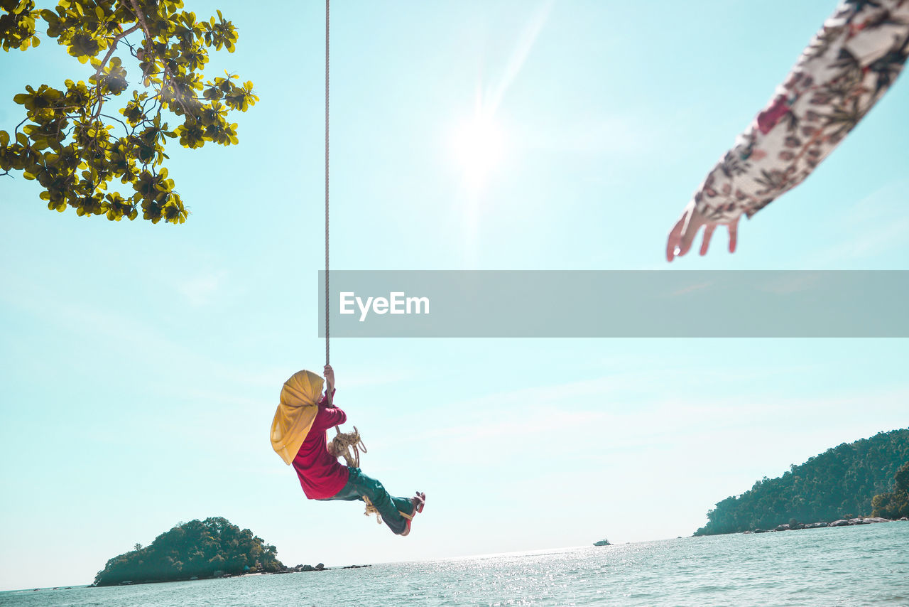 Low angle view of girl on rope swing over ocean