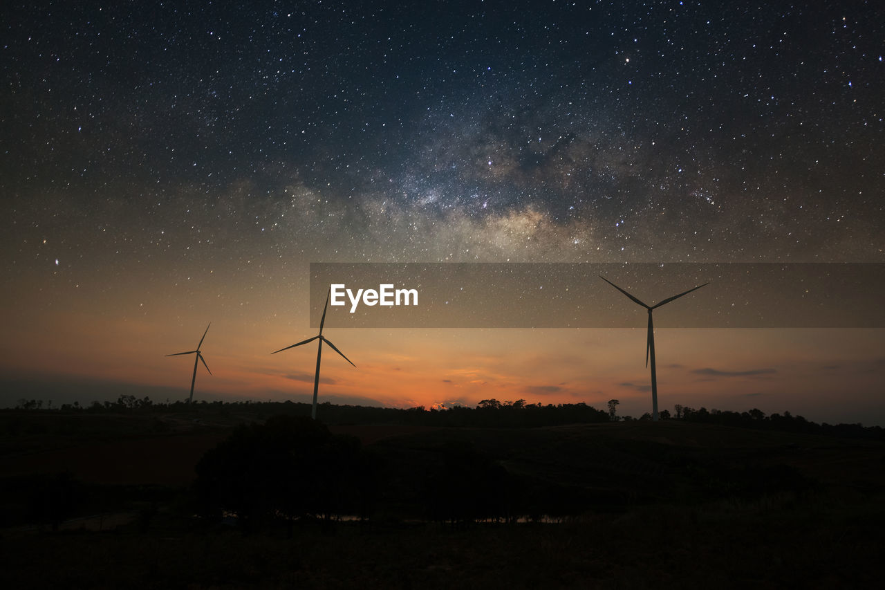 Silhouette wind turbines on field against sky at night