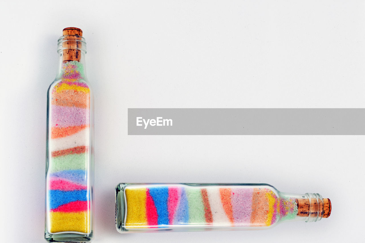 Close-up of colorful sand in bottles on white background