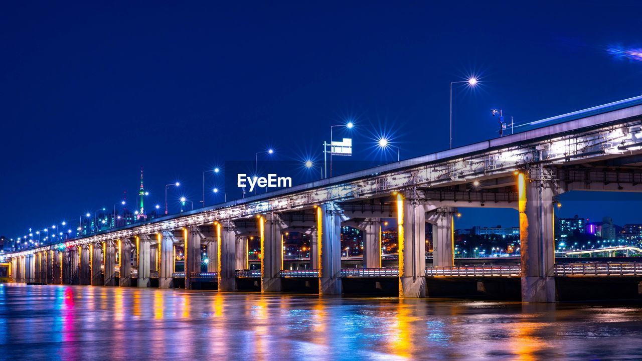 Illuminated bridge over river against sky at night