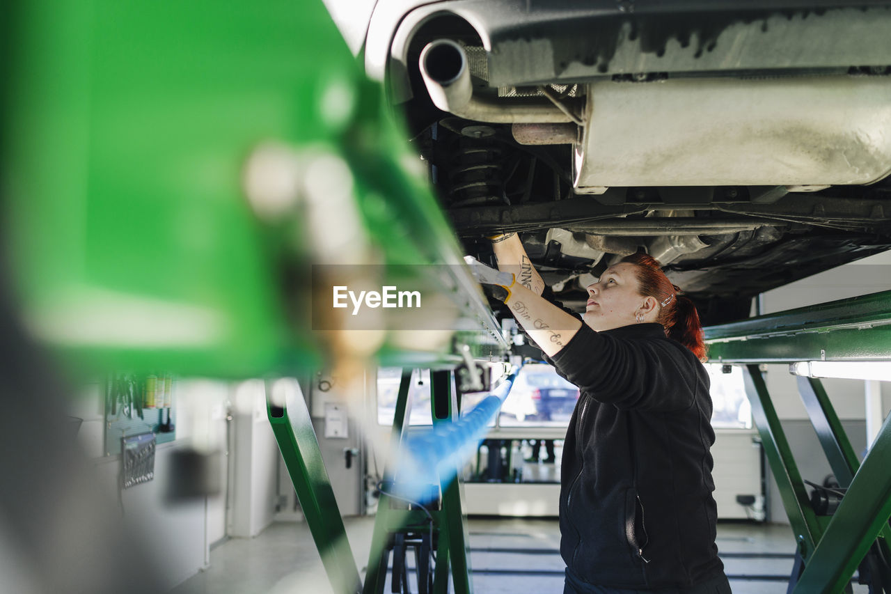 Side view of female mechanic repairing car on hydraulic lift