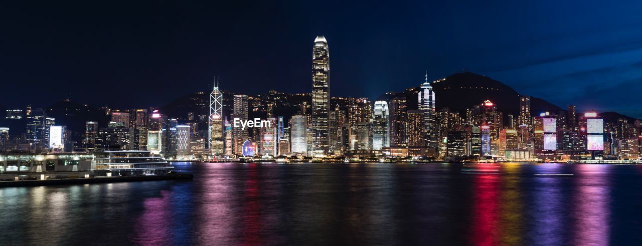 Panoramic shot of illuminated city by river at night