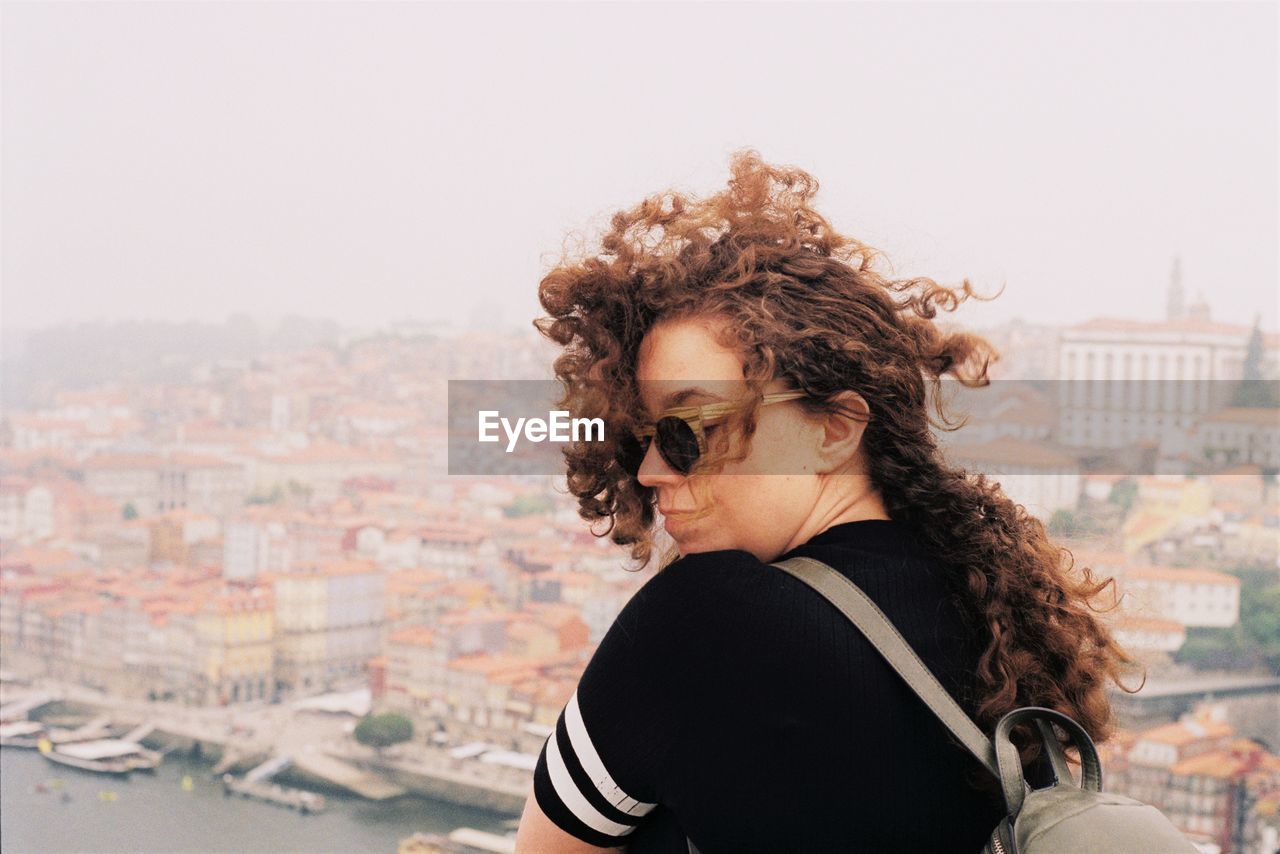 Portrait of girl with flowing curly hair standing against cityscape