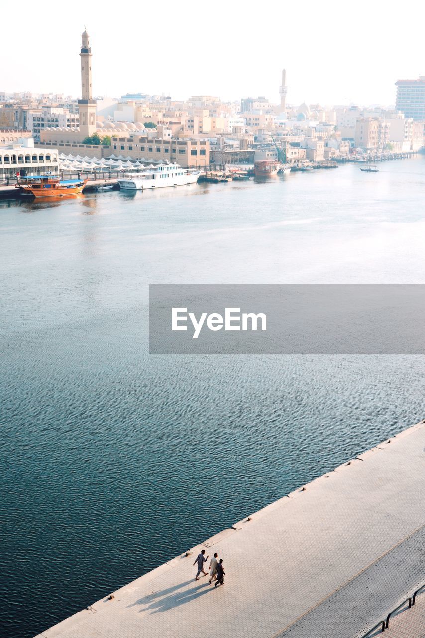 High angle view of people walking on footpath by sea and buildings against sky